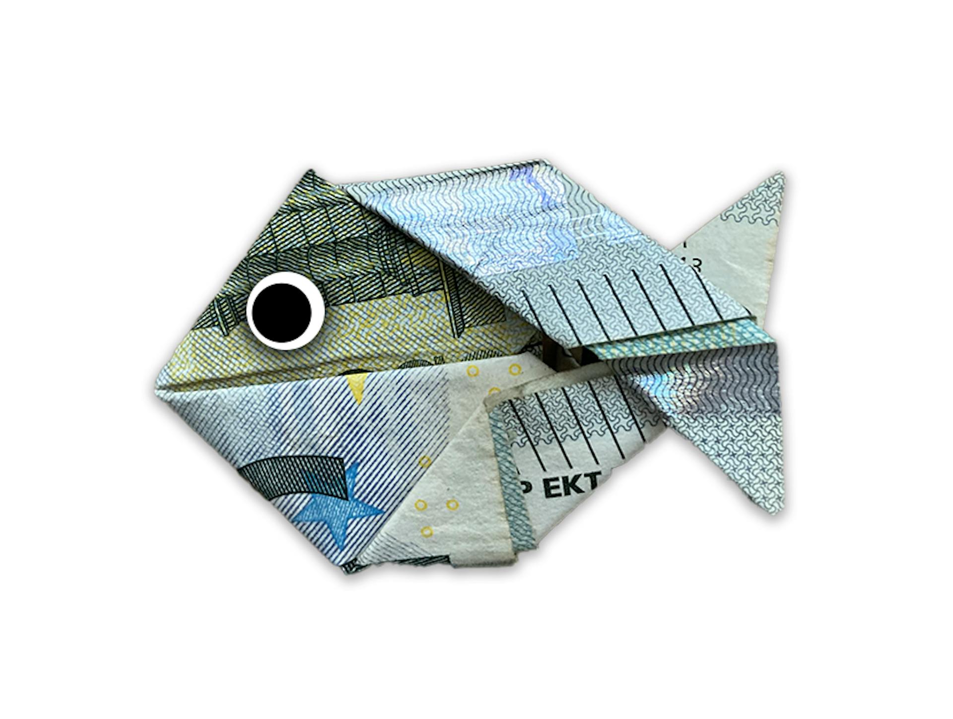 Ein Geldschein in Form eines Fisches, kunstvoll gefaltet, dient als kreative Anspielung auf einzigartige Geldgeschenke.
