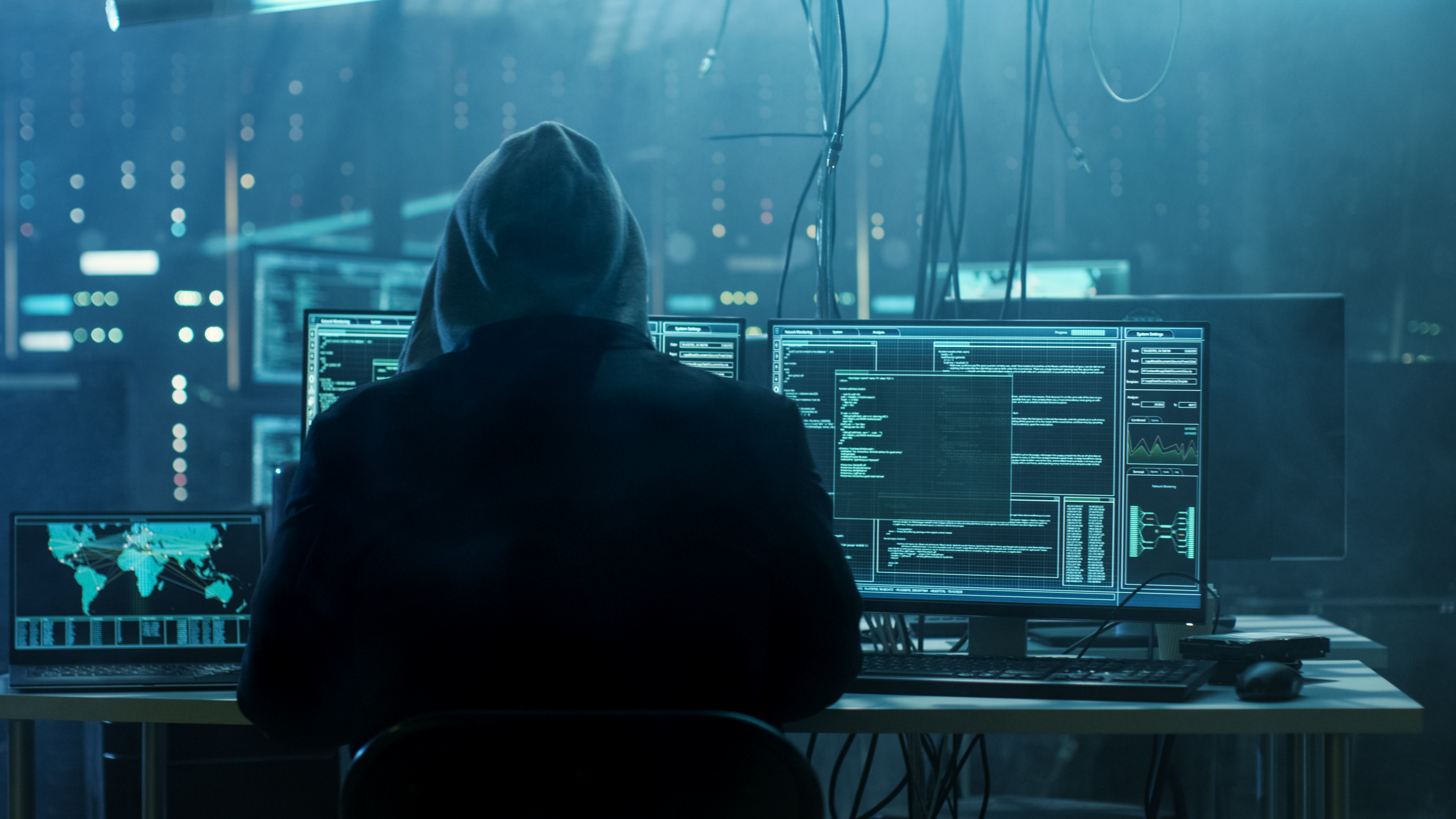 Phishing-Betrüger*in sitzt vor mehreren Bildschirmen mit sensiblen Daten in einem dunklen Serverraum.