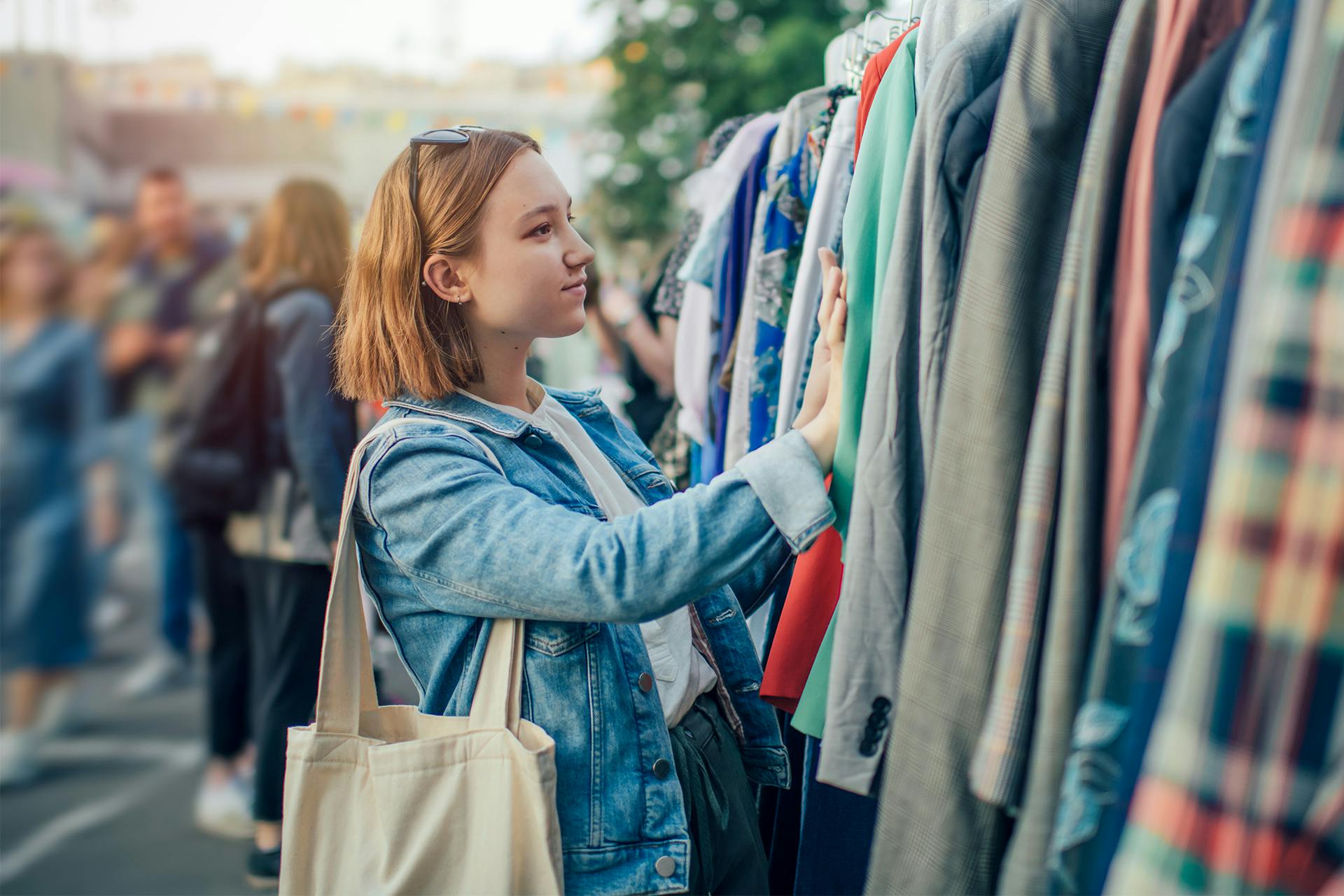 Eine junge Frau betrachtet neugierig die Kleidungsstücke an einer Kleiderstange.