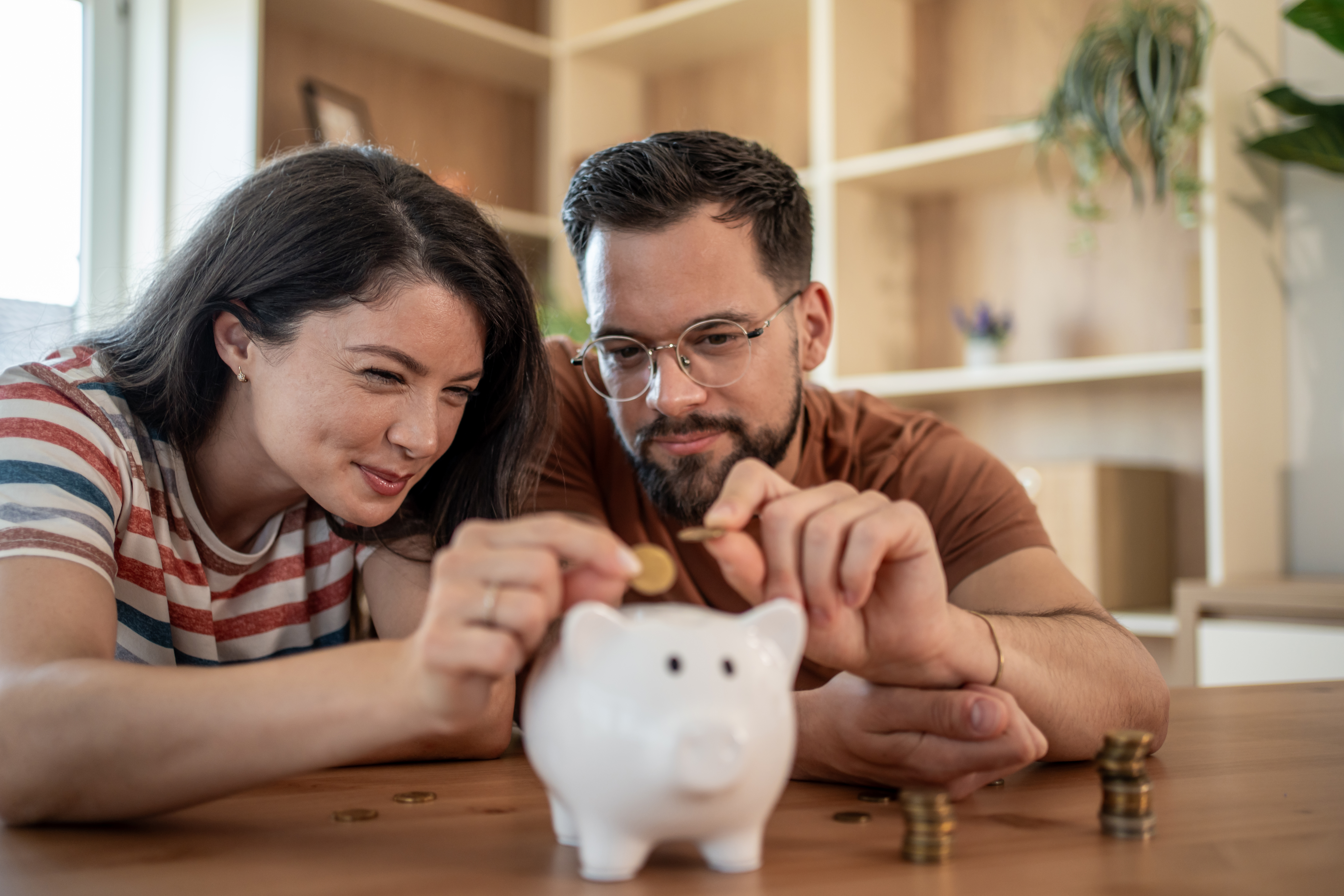 Pärchen wirft gemeinsam Geld in ein Sparschwein am Weltspartag.
