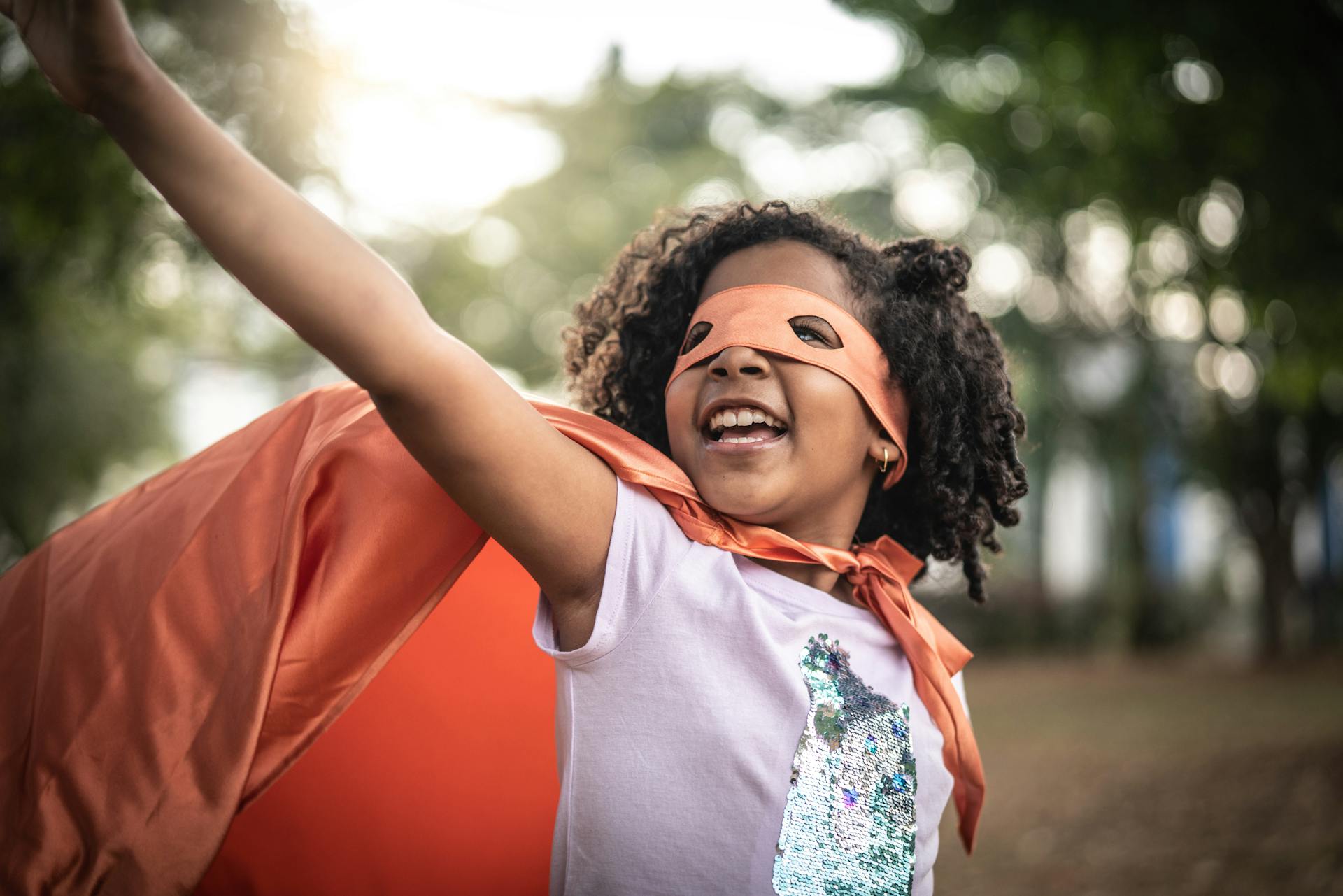 Ein Mädchen, als Superheldin verkleidet mit Cape und Maske, symbolisiert das Thema Frauen und Finanzen.